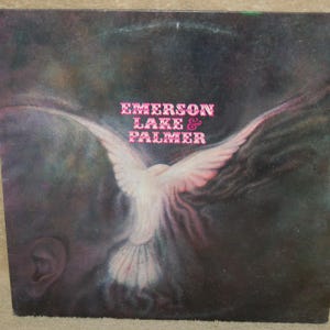 May include: A vintage vinyl record album cover featuring a white dove with pink wings against a dark background. The album title "Emerson Lake & Palmer" is printed in pink letters.