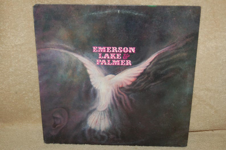 May include: A vintage vinyl record album cover featuring a white dove with pink wings against a dark background. The album title "Emerson Lake & Palmer" is printed in pink letters.
