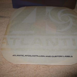 Pu&ograve; includere: Un'etichetta traslucida di forma quadrata con la parola "ATLANTIC" ben visibile. L'etichetta presenta anche un design a spirale e il testo "ATLANTIC, ATCO, COTILLION AND CUSTOM LABELS" in un carattere pi&ugrave; piccolo.