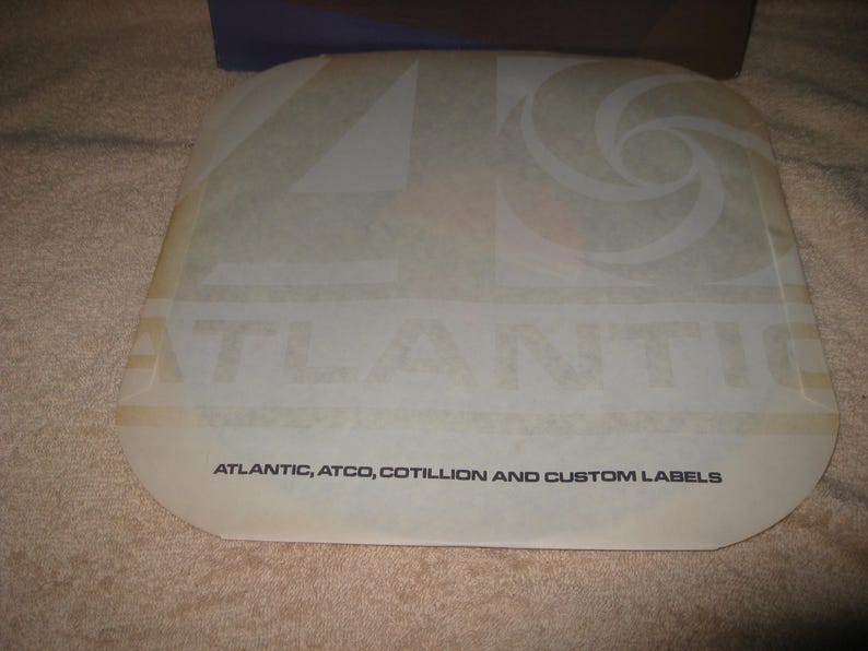 Pu&ograve; includere: Un'etichetta traslucida di forma quadrata con la parola "ATLANTIC" ben visibile. L'etichetta presenta anche un design a spirale e il testo "ATLANTIC, ATCO, COTILLION AND CUSTOM LABELS" in un carattere pi&ugrave; piccolo.