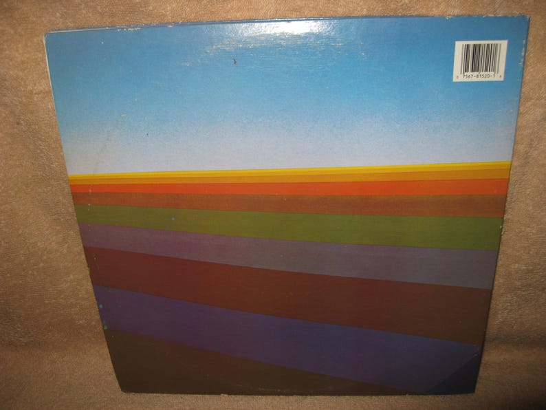 Pu&ograve; includere: Una copertina di un album vintage con un design sfumato. La parte superiore &egrave; un cielo azzurro chiaro, che sfuma in un orizzonte di strisce arancioni, gialle e verdi. Sotto, strisce angolate in tonalit&agrave; marroni, viola e blu creano un effetto a strati. Un codice a barre &egrave; visibile.