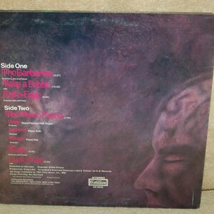 May include: Back cover of a vinyl record album with a black and white photo of a person's face. The album is titled "The Barbarians" and includes the song titles "Take a Pebble" and "Love-Elf".