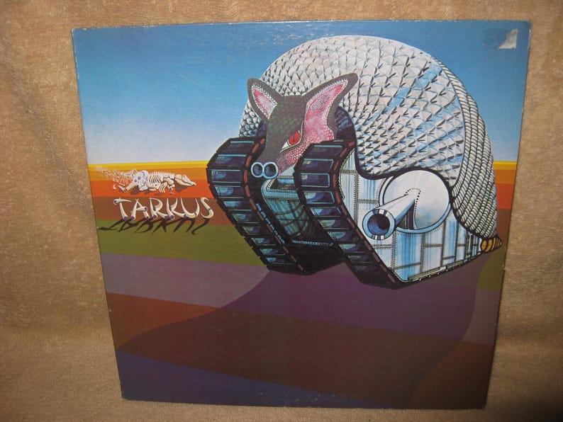 Pu&ograve; includere: Copertina dell'album con un'illustrazione surreale di una creatura simile a un carro armato con un guscio simile a un armadillo. La creatura ha una faccia rosa e occhi rossi. Il titolo dell'album "Tarkus" &egrave; scritto in testo stilizzato su uno sfondo colorato.