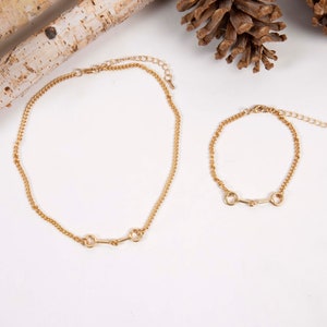 May include: A set of two gold-toned necklaces with a simple chain design and a horse bit pendant. The necklace on the left is longer than the necklace on the right.