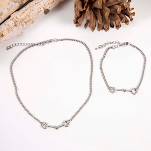 May include: A silver necklace and bracelet set with a simple, elegant design. The necklace and bracelet feature a small, silver horse bit charm.