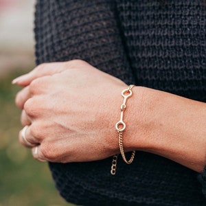 May include: A gold chain bracelet with a simple, open circle design. The bracelet is made of a delicate chain and has a secure clasp.