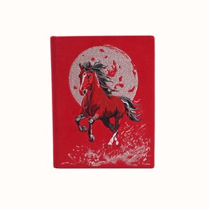 Könnte beinhalten: Rotes Notizbuch mit einem gestickten Bild eines steigenden roten Pferdes mit schwarzer Mähne und Schweif, vor einem silbernen Mond. Das Pferd hat weiße Akzente, die ein dynamisches und künstlerisches Design schaffen.