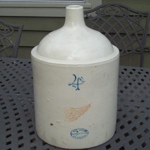 May include: A cylindrical off-white stoneware jug with a narrow neck. The front features a blue number 4, a stamped red wing logo, and a blue oval mark that reads Red Wing Union Stoneware Co. Red Wing, Minn. The surface has minor imperfections.