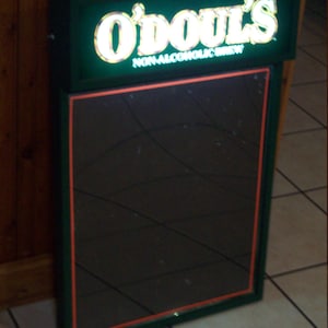 May include: A green and black sign with a mirror. The sign has the words "O'Doul's Non-Alcoholic Brew" in white letters.