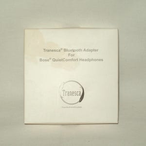 May include: A white square box with the text "Tranesca Bluetooth Adapter For Bose QuietComfort Headphones". The box has a circular logo with the name "Tranesca" and the tagline "Transform and Escalate".