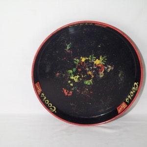 May include: A black metal serving tray with a red rim and a floral design in the centre. The tray has the words "Goetz Beer" printed on the rim in yellow.