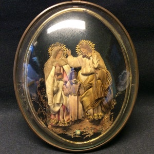 Un antiguo diorama francés del siglo XIX, en marco ovalado de vidrio condenado, imagen relicario de la Santa Madre María, José y el Niño Jesús.