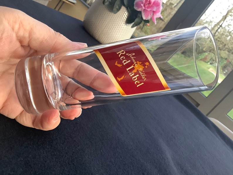 May include: A clear glass shot glass with a red and gold label that reads "Johnnie Walker Red Label".