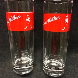 May include: Two clear glass tumblers with a red band around the middle. The band has the words "Johnnie Walker" in white lettering and a white silhouette of a man walking with a cane.