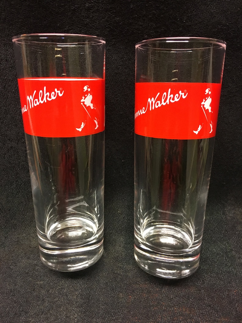 May include: Two clear glass tumblers with a red band around the middle. The band has the words "Johnnie Walker" in white lettering and a white silhouette of a man walking with a cane.