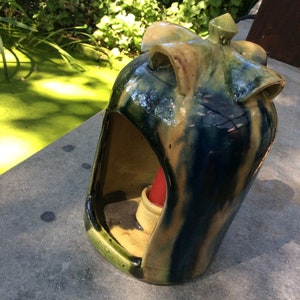 May include: A blue and brown ceramic candle holder with a unique design. The holder has a large opening at the top and a smaller opening at the bottom for the candle.