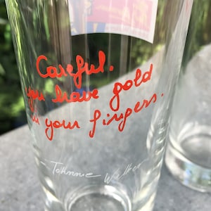 May include: A clear glass with a red handwritten message that says "Careful! You leave gold in your fingers." The glass has a white signature at the bottom that says "Tommie Walker".
