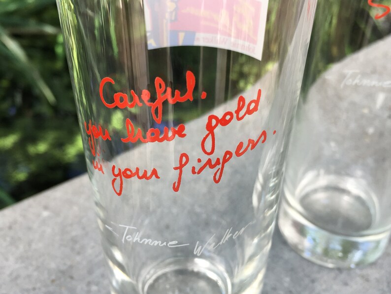 May include: A clear glass with a red handwritten message that says "Careful! You leave gold in your fingers." The glass has a white signature at the bottom that says "Tommie Walker".