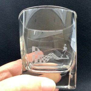May include: A clear glass tumbler with a square base. The glass has an etched design of a chequered flag and a person running with the text "Keep" below the design.