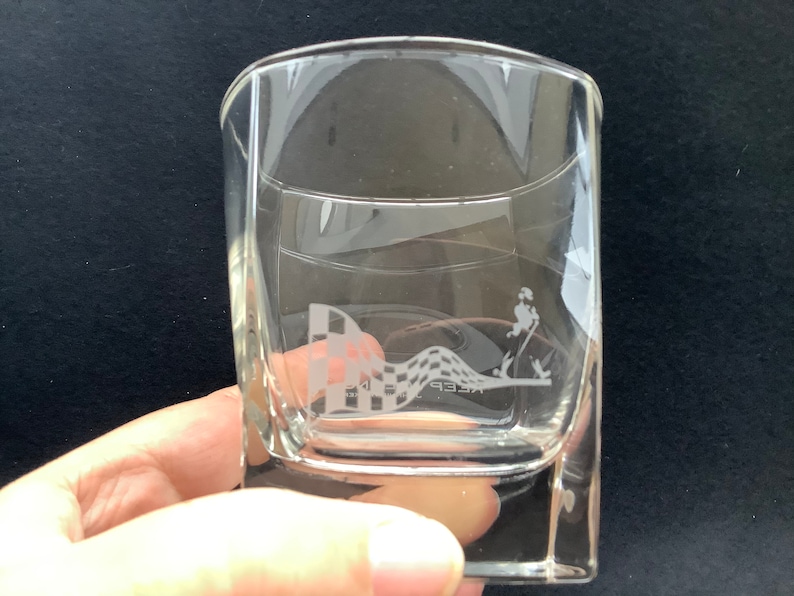 May include: A clear glass tumbler with a square base. The glass has an etched design of a chequered flag and a person running with the text "Keep" below the design.
