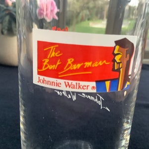 May include: A clear glass with a red, white, and blue sticker that says "The Boat Barman Johnnie Walker&reg;" with a cartoon illustration of a man's head.