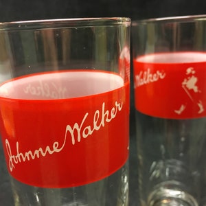 May include: Two clear glass tumblers with a red band around the middle. The band has white lettering that says "Johnnie Walker".