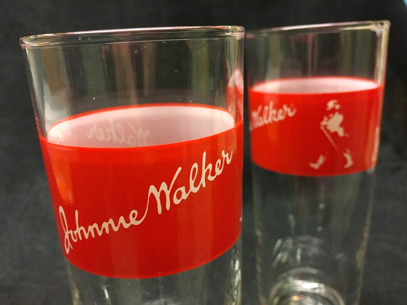 May include: Two clear glass tumblers with a red band around the middle. The band has white lettering that says "Johnnie Walker".