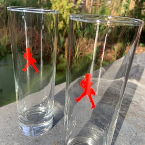 Op de afbeelding: Twee heldere glazen highball-glazen met een rood lopend man-logo op elk.