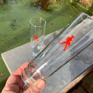 Op de afbeelding: Twee heldere glazen drinkglazen met een rood lopend figuurlogo aan de zijkant.