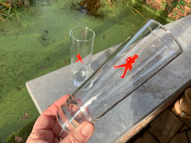 Op de afbeelding: Twee heldere glazen drinkglazen met een rood lopend figuurlogo aan de zijkant.