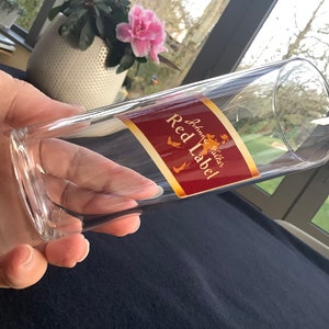 May include: A clear glass tumbler with a red and gold label that reads "Johnnie Walker Red Label".