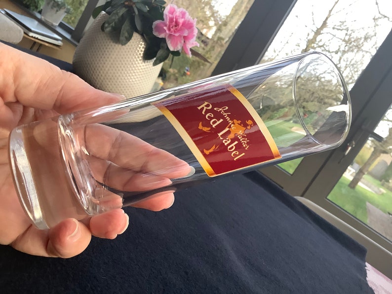 May include: A clear glass tumbler with a red and gold label that reads "Johnnie Walker Red Label".