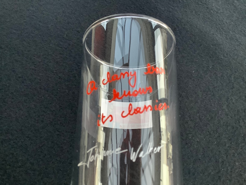 May include: A clear glass with red writing that says "A classy bar knows it's classics." The writing is signed "Tom Hanks Walker".