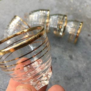 Puede incluir: Juego de vasos de chupito de cristal transparente con rayas horizontales doradas y bordes dorados. Los vasos tienen una base facetada. Estos vasos de chupito vintage son adecuados para servir licores.
