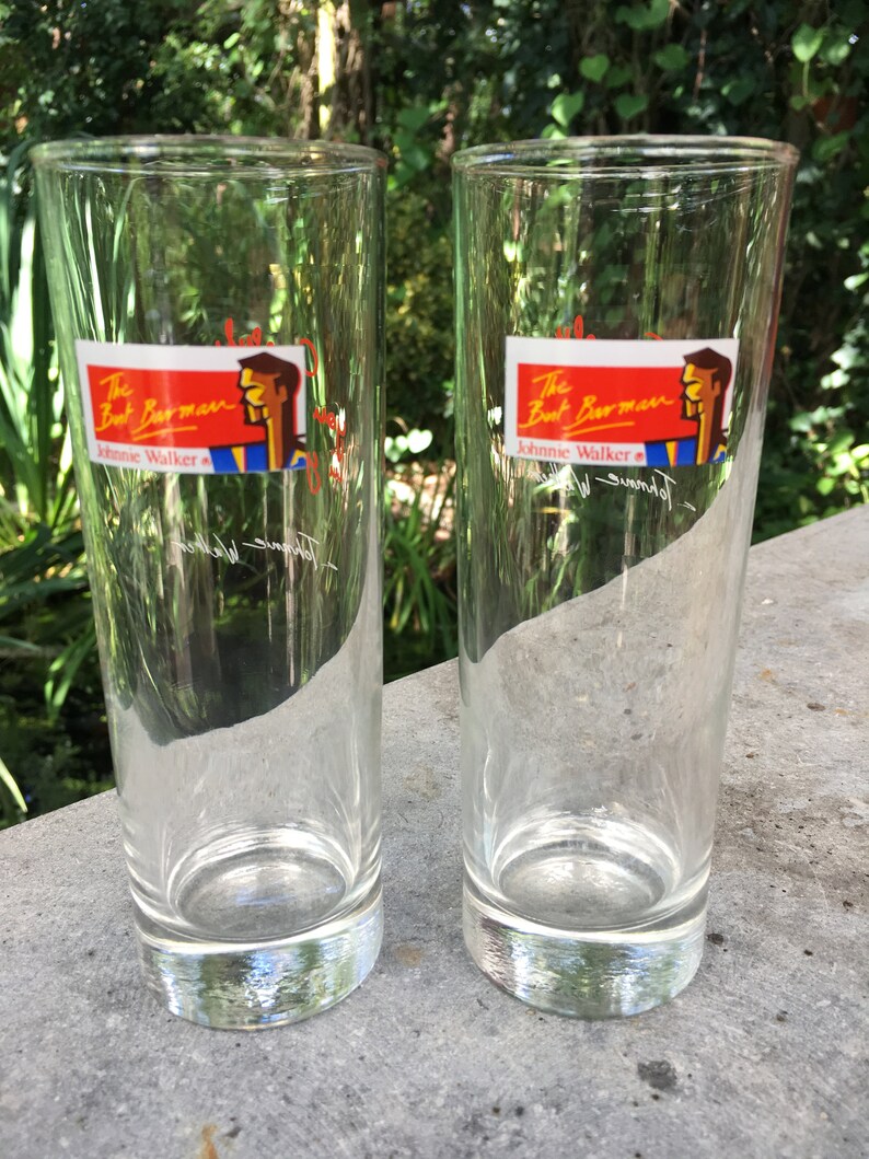 May include: Two clear glass highball glasses with a red and yellow label that reads "The Best Barman Johnnie Walker" with a cartoon illustration of a man.