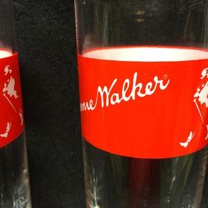May include: Two clear glass tumblers with a red band around the top. The band has the words "Johnnie Walker" in white lettering and a white silhouette of a man walking with a cane.