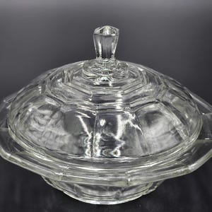 Könnte beinhalten: Eine klare, antike Butterdose aus Glas mit Deckel. Die Schale und der Deckel weisen ein geometrisches, facettiertes Design auf. Der Deckel hat einen kleinen, rautenförmigen Griff. Die Schale stammt wahrscheinlich aus der Mitte des 20. Jahrhunderts.