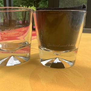 May include: Two clear double-walled drinking glasses with a geometric base design. One glass is empty, the other contains a dark liquid and a folded black napkin. The text "Our blend cannot be beat" is visible on the glass.