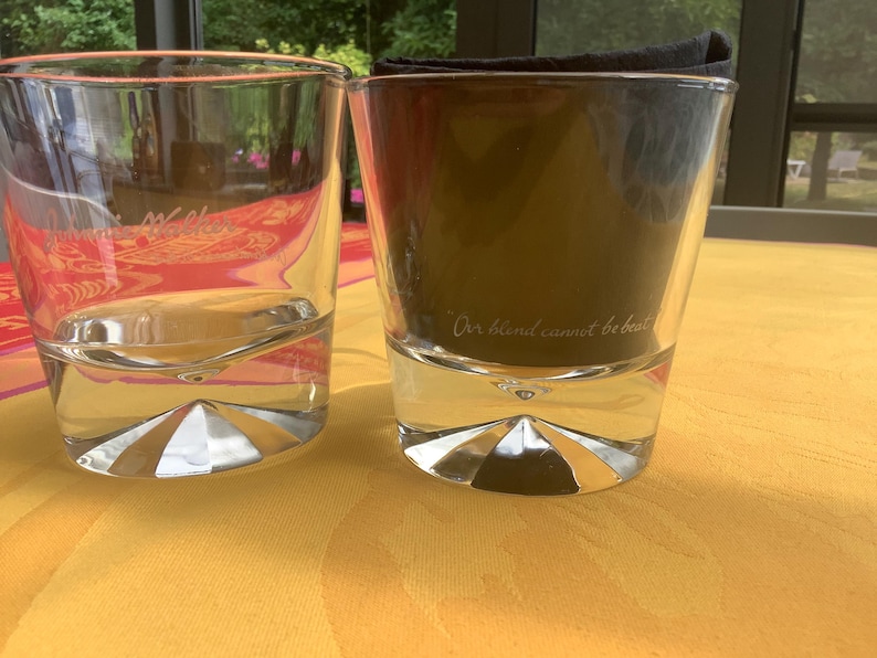 May include: Two clear double-walled drinking glasses with a geometric base design. One glass is empty, the other contains a dark liquid and a folded black napkin. The text "Our blend cannot be beat" is visible on the glass.