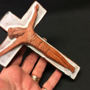 Może przedstawiać: Ceramiczny krucyfiks z białym tłem i brązową figurą Jezusa. Krucyfiks jest pokryty zielono-białą glazurą.
