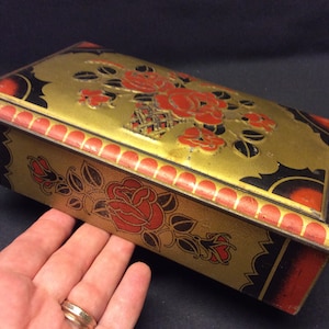 Vintage rectangular tin with embossed roses in a vase on the hinged lid, in gold, red, and black colors. Red roses.