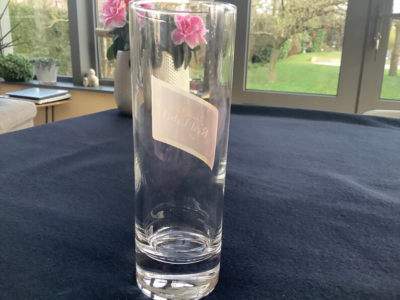 May include: A clear glass tumbler with a white label that says "Red Bull" on it.