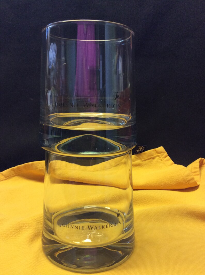 May include: A clear glass tumbler with the Johnnie Walker logo printed on the bottom. The glass has a double layer design.