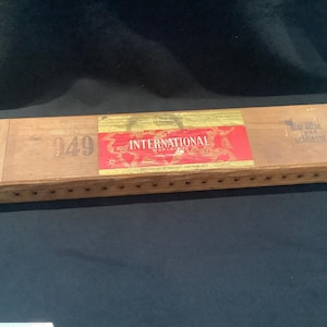 May include: A wooden box with a label that reads "International" and "949". The box is made of light brown wood and has a gold trim. The label is red, white, and gold.