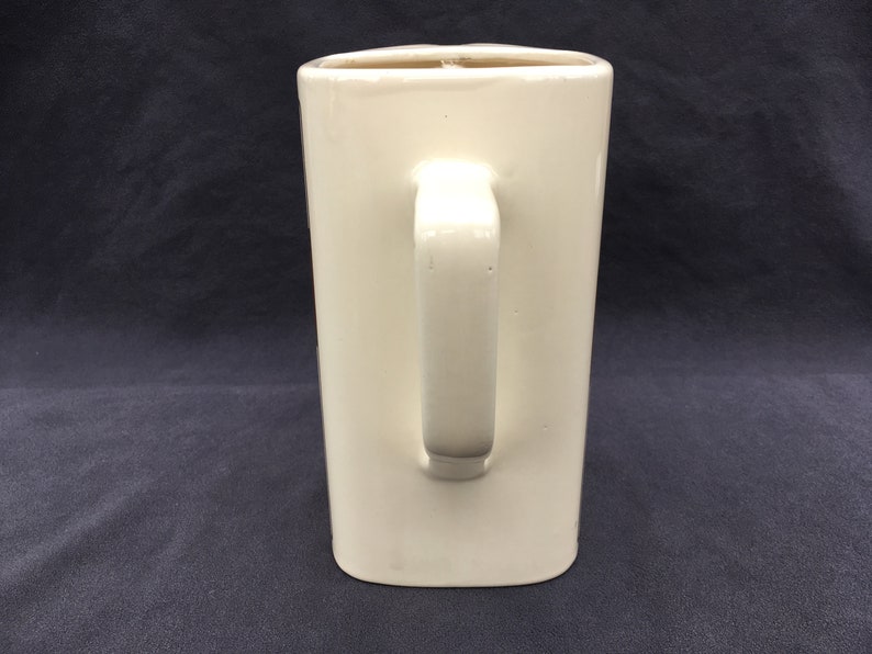 Pode incluir: Uma caneca retangular de cer&acirc;mica creme com uma al&ccedil;a. A caneca tem um acabamento liso e brilhante e um design simples e minimalista. A al&ccedil;a &eacute; fixada na lateral da caneca. A caneca tem aproximadamente 15 cm de altura.