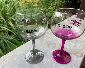 Könnte beinhalten: Zwei klare Bulldog London Dry Gin Gläser. Eines hat einen klaren Stiel und eine klare Schale, das andere einen rosa Stiel und eine rosa Schale. Das Bulldog-Logo und die Union Jack-Flagge sind auf den Gläsern aufgedruckt.