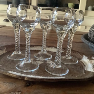 Könnte beinhalten: Sechs klare Glas-Stielgläser mit einem gedrehten Stieldesign sind auf einem silbernen Tablett mit einem verzierten Design angeordnet.