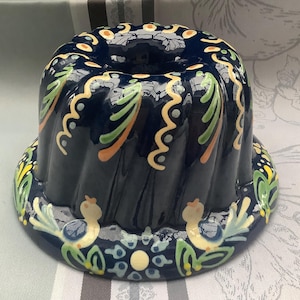 Pode incluir: Uma forma de bolo bundt de cerâmica azul com um design floral colorido. A forma apresenta um padrão de espiral e dois pássaros na borda inferior.