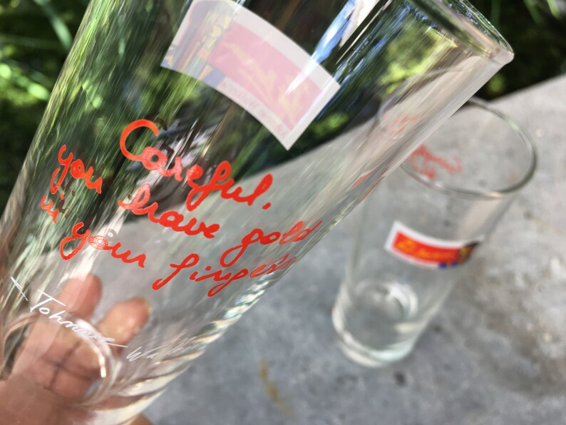 May include: Two clear glass drinking glasses. One glass has the words "Careful. You have got your fingers" written in red marker.
