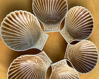 May include: Set of six brown and white ceramic seashell-shaped dishes. The dishes are arranged in a circle, with the opening of each shell facing outward.